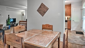 A dining area with a wooden table and chairs, a television in the background, and a kitchen visible through an open doorway. - San Antonio Home w/ Pvt. Yard, 5 Mi to Downtown! (San Antonio)