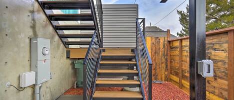 Una escalera moderna con barandillas de metal y escalones de madera, que conduce a un espacio cubierto con vistas al cielo.