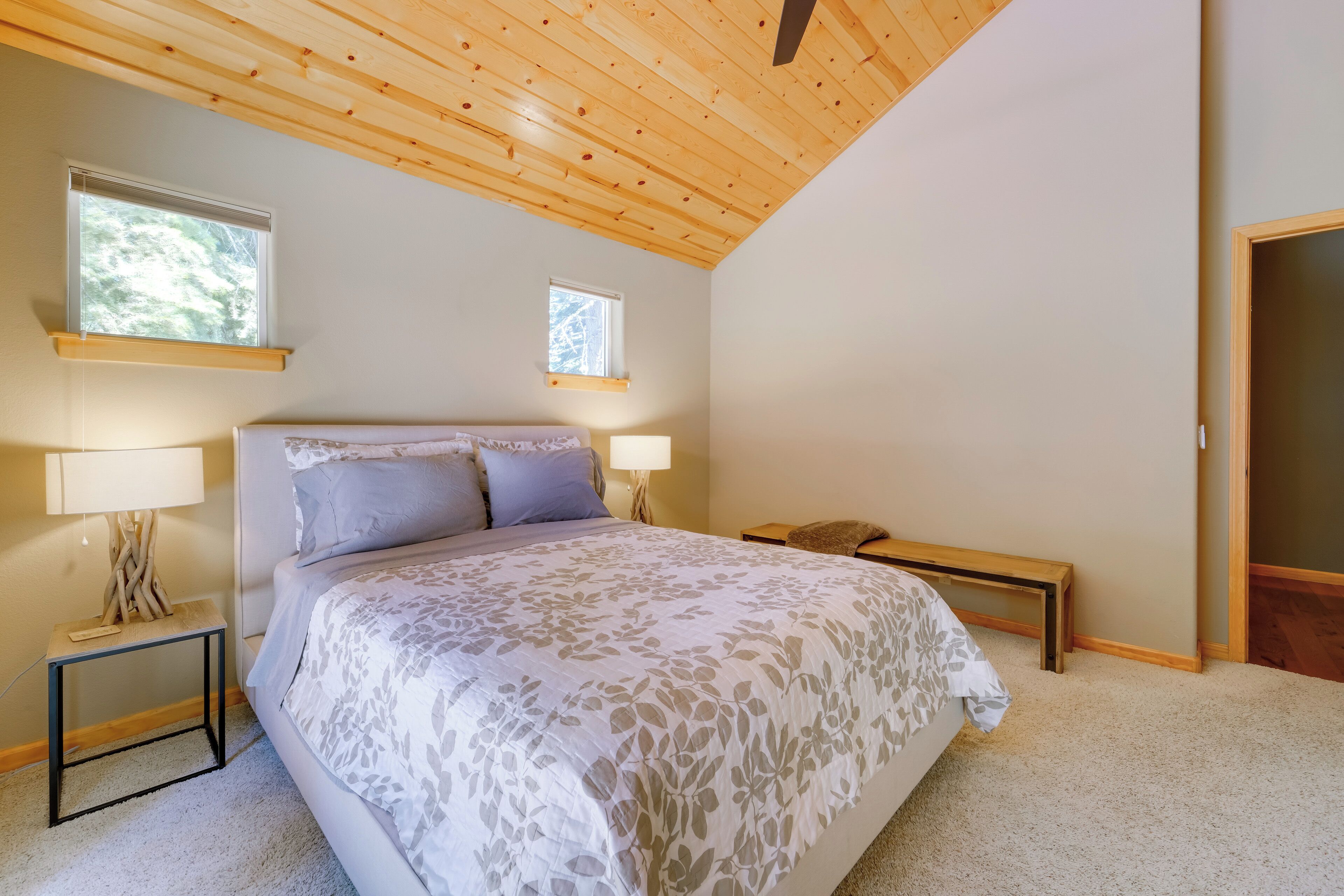 A bedroom with a large bed, two bedside tables with lamps, a bench, and a window.