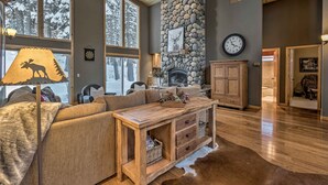Una sala de estar acogedora con chimenea de piedra, ventanas amplias y techo de madera.