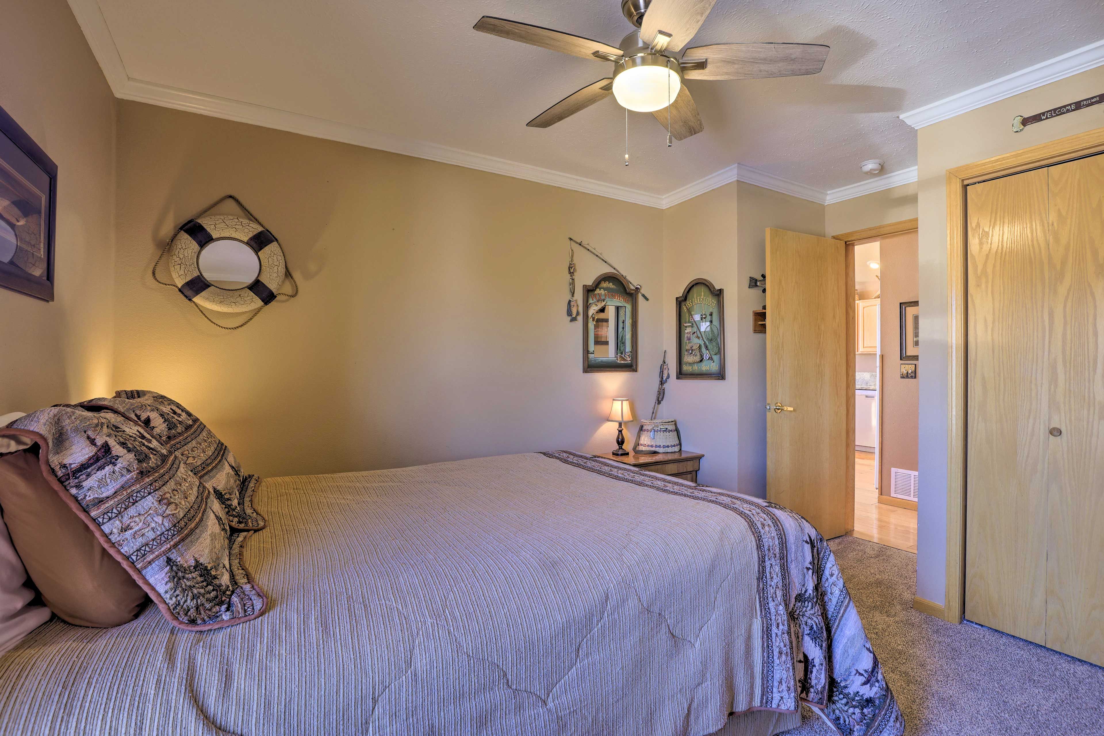 A bedroom with a bed, a ceiling fan, a wall-mounted lamp, and a door leading to another room.