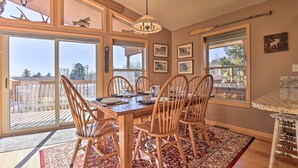 A dining area with a wooden table and chairs, large windows, and a chandelier.
