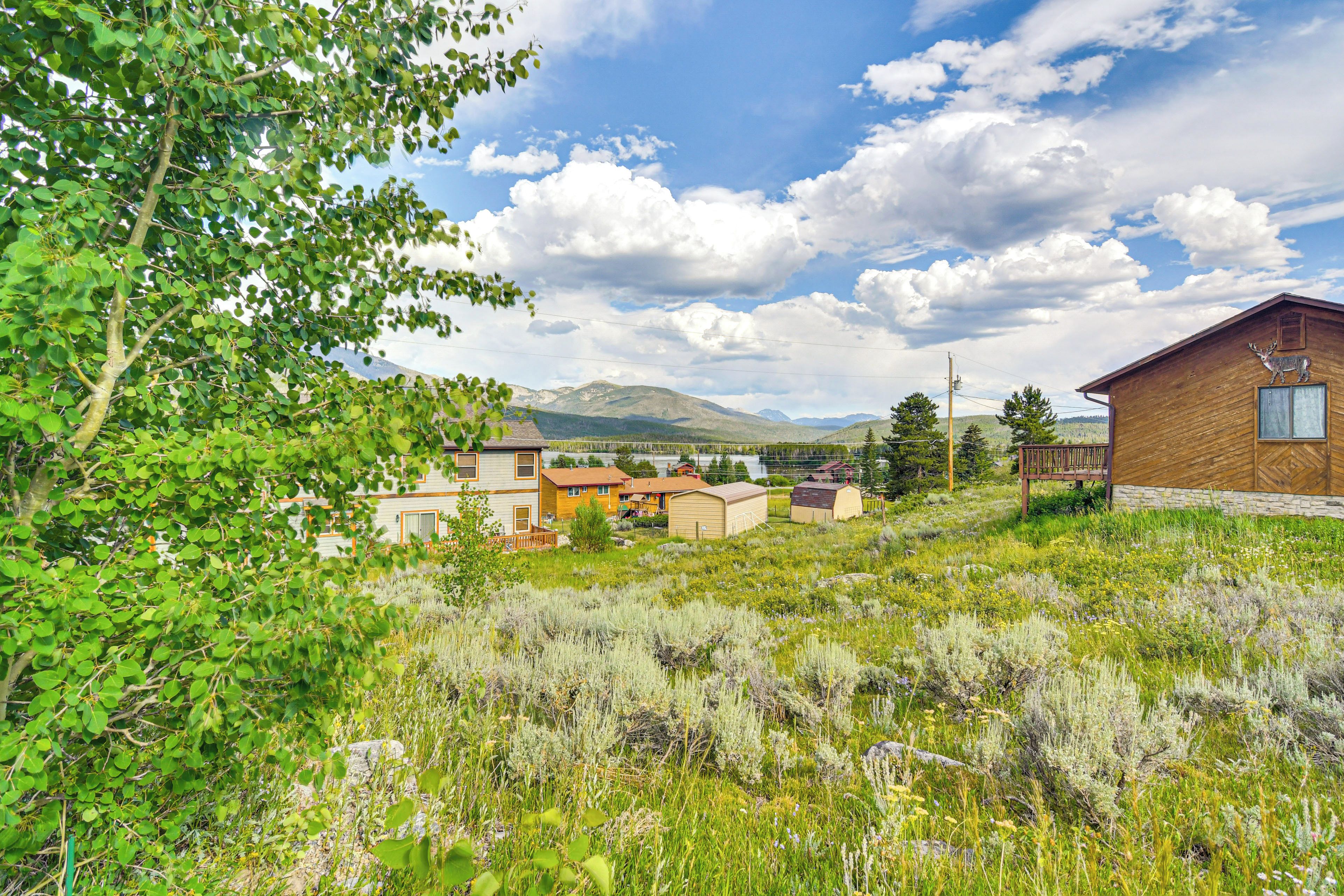A rural landscape with a wooden cabin and several houses, surrounded by lush greenery and mountains in the background.