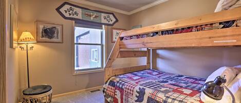 A bedroom with a bunk bed, a small round stool, a lamp, and a window with a view of a building.
