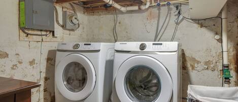 Two Samsung washing machines in a room with a wooden ceiling and exposed pipes.
