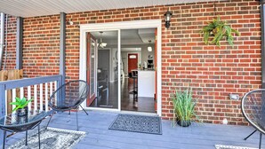 A covered patio with a brick wall, a sliding glass door leading to a kitchen, and two black chairs with potted plants. - Chic Townhome w/ Deck: 6 Mi to Dtwn Baltimore (Baltimore)