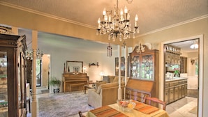 Een ruime woonkamer met een kroonluchter, een eethoek met een tafel gedekt voor twee personen, en een zichtbare keuken via een open doorgang.