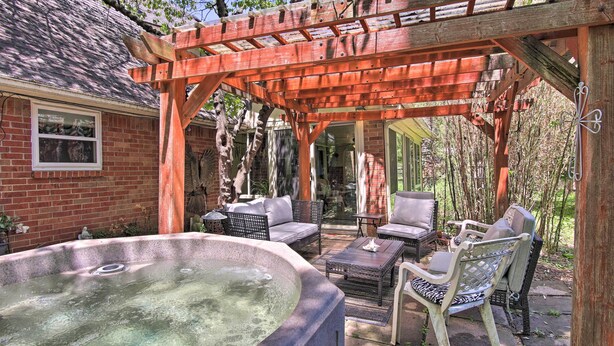 Een overdekt terras met een jacuzzi, tuinmeubilair en een houten pergola.
