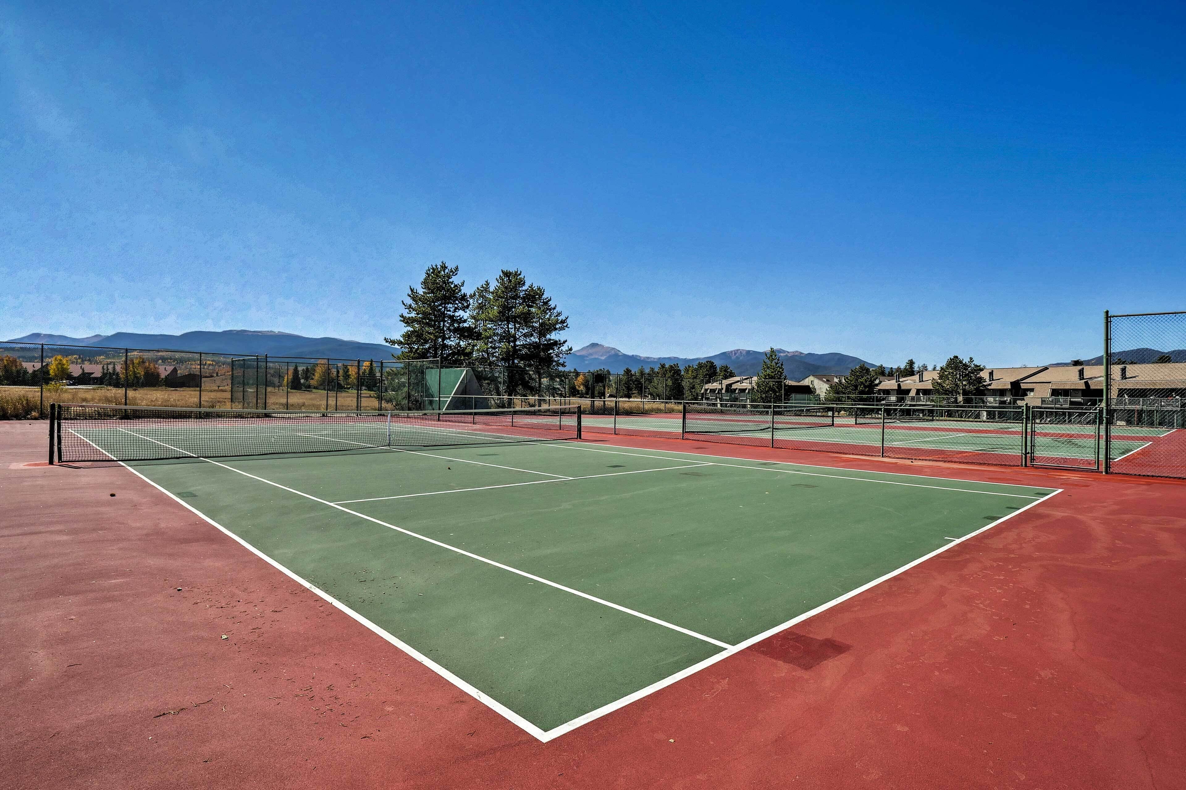 A tennis court with a net, surrounded by a fence, and mountains in the background.