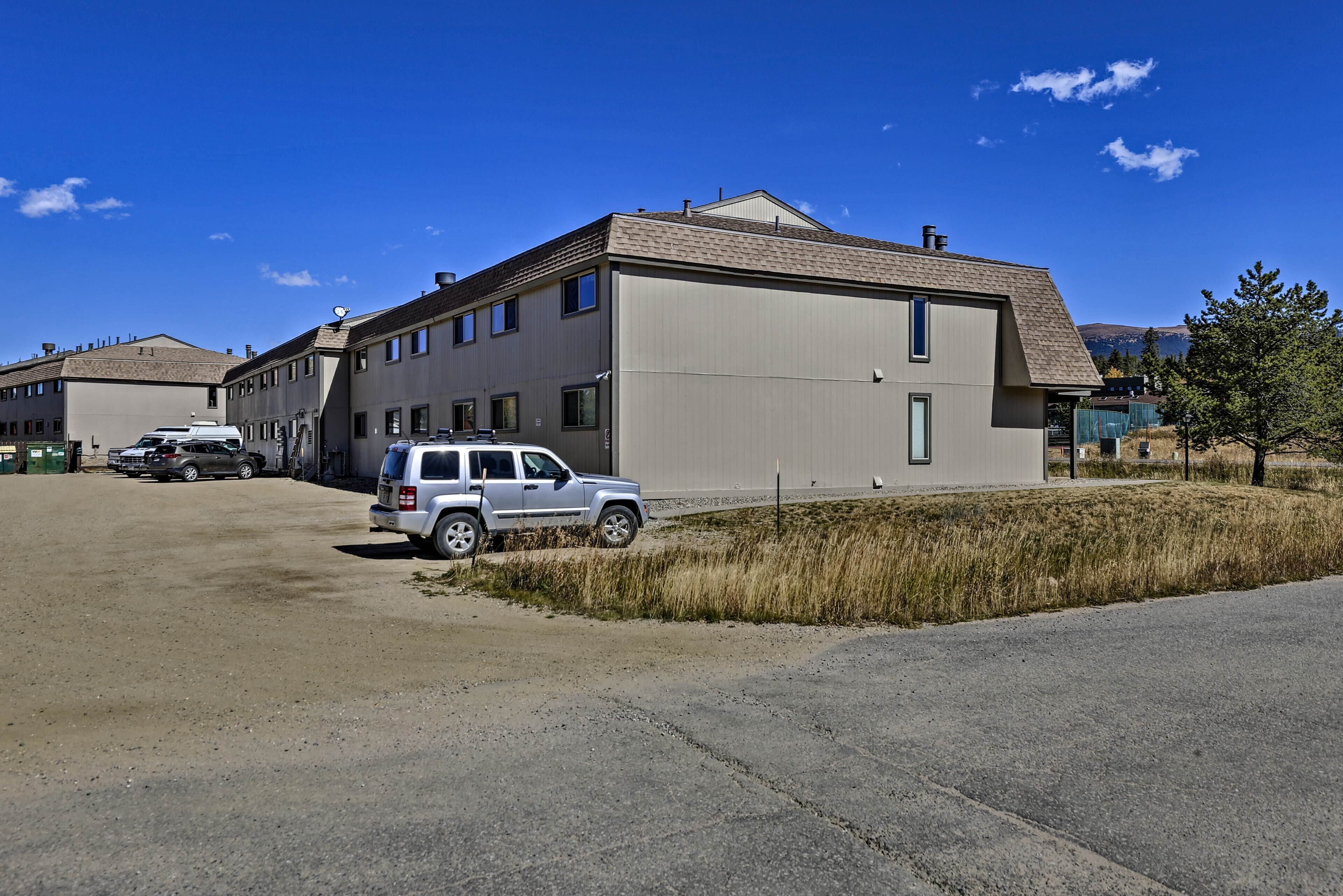 A modern building with a flat roof and multiple windows, located in a parking lot with a few vehicles.