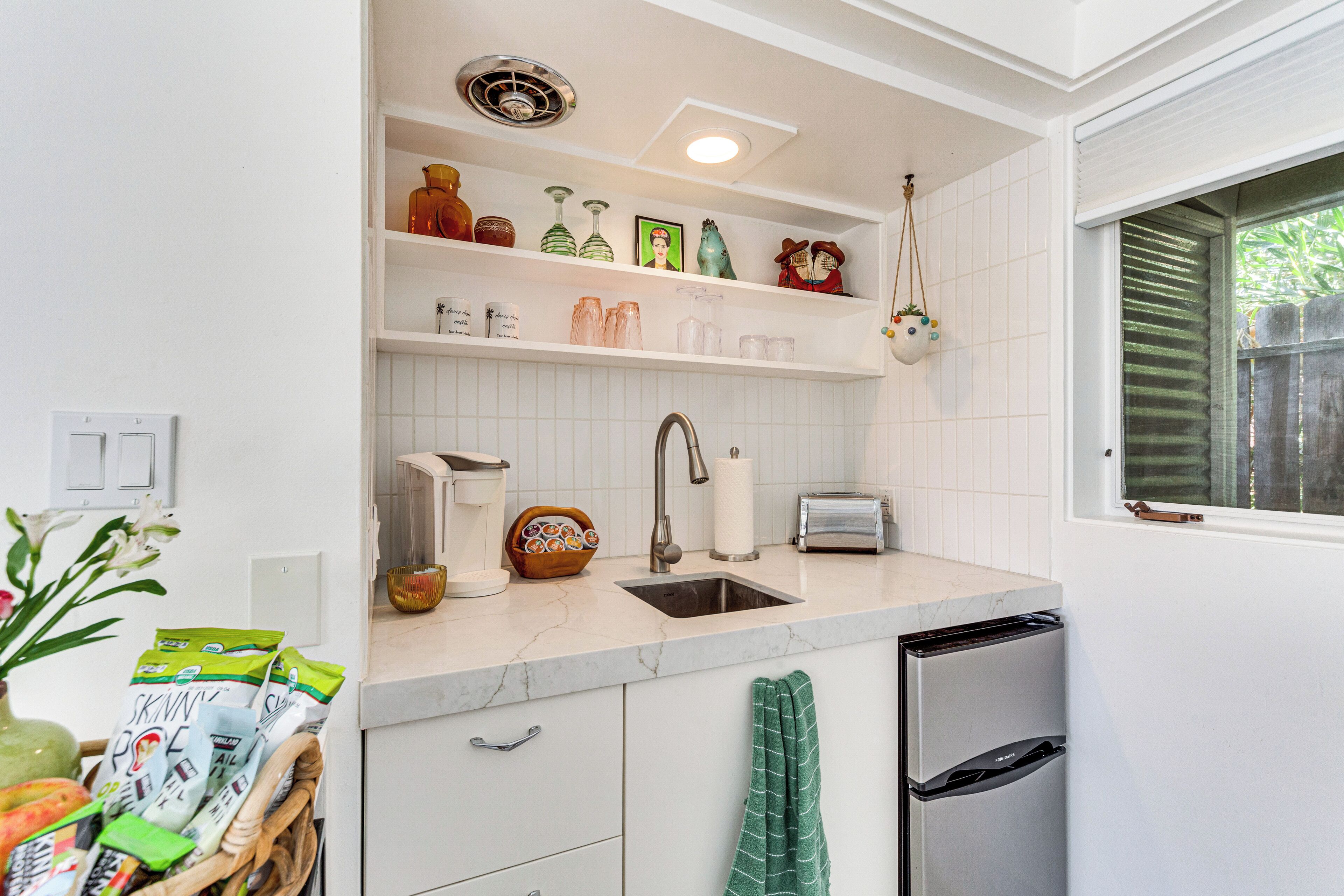 A kitchen with white cabinets, a marble countertop, a sink, a toaster, and a hanging pot rack.