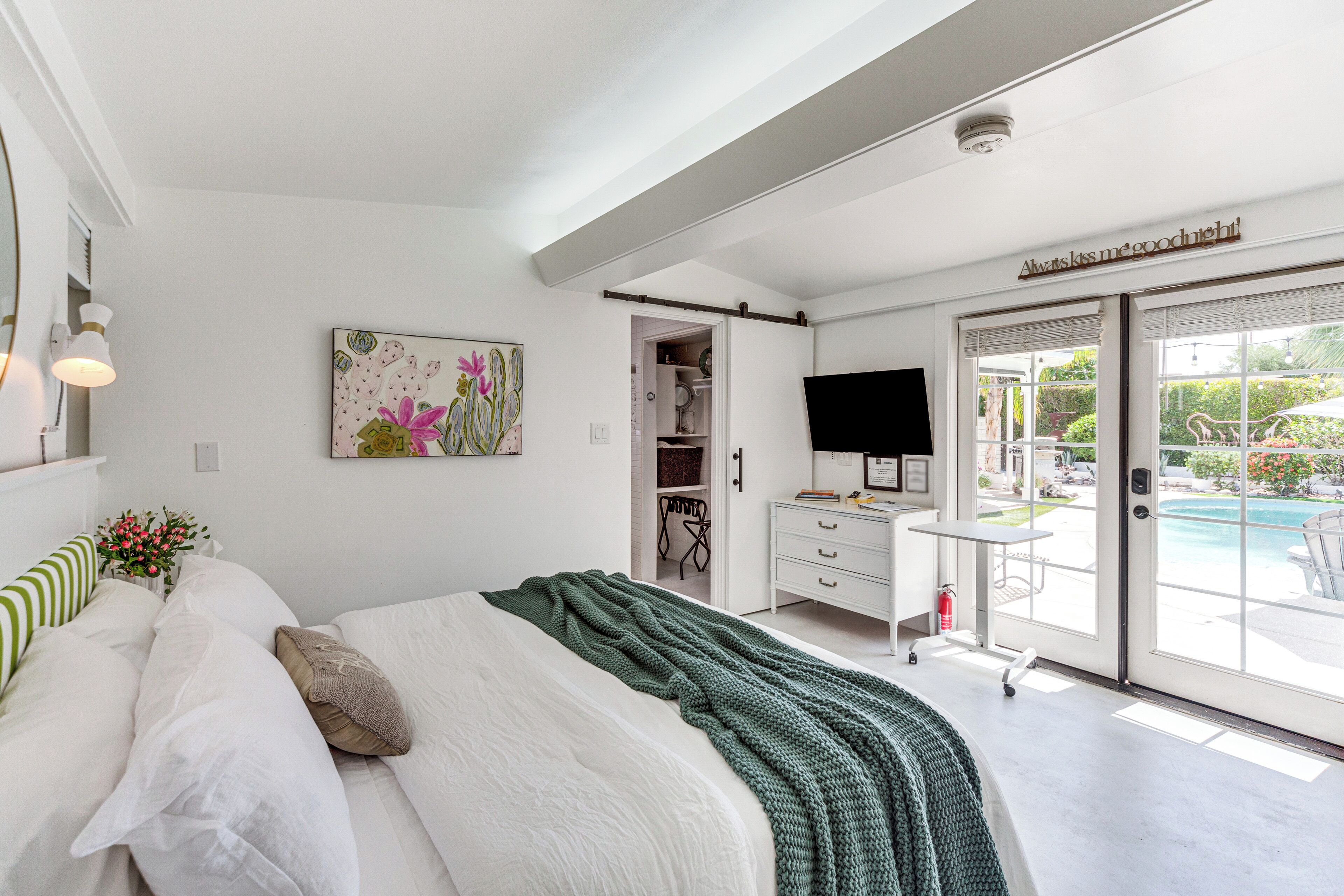 Ein Schlafzimmer mit einem Bett, einem Bild, einem Fernseher und einer Schiebetür zu einem Balkon mit einem Pool.