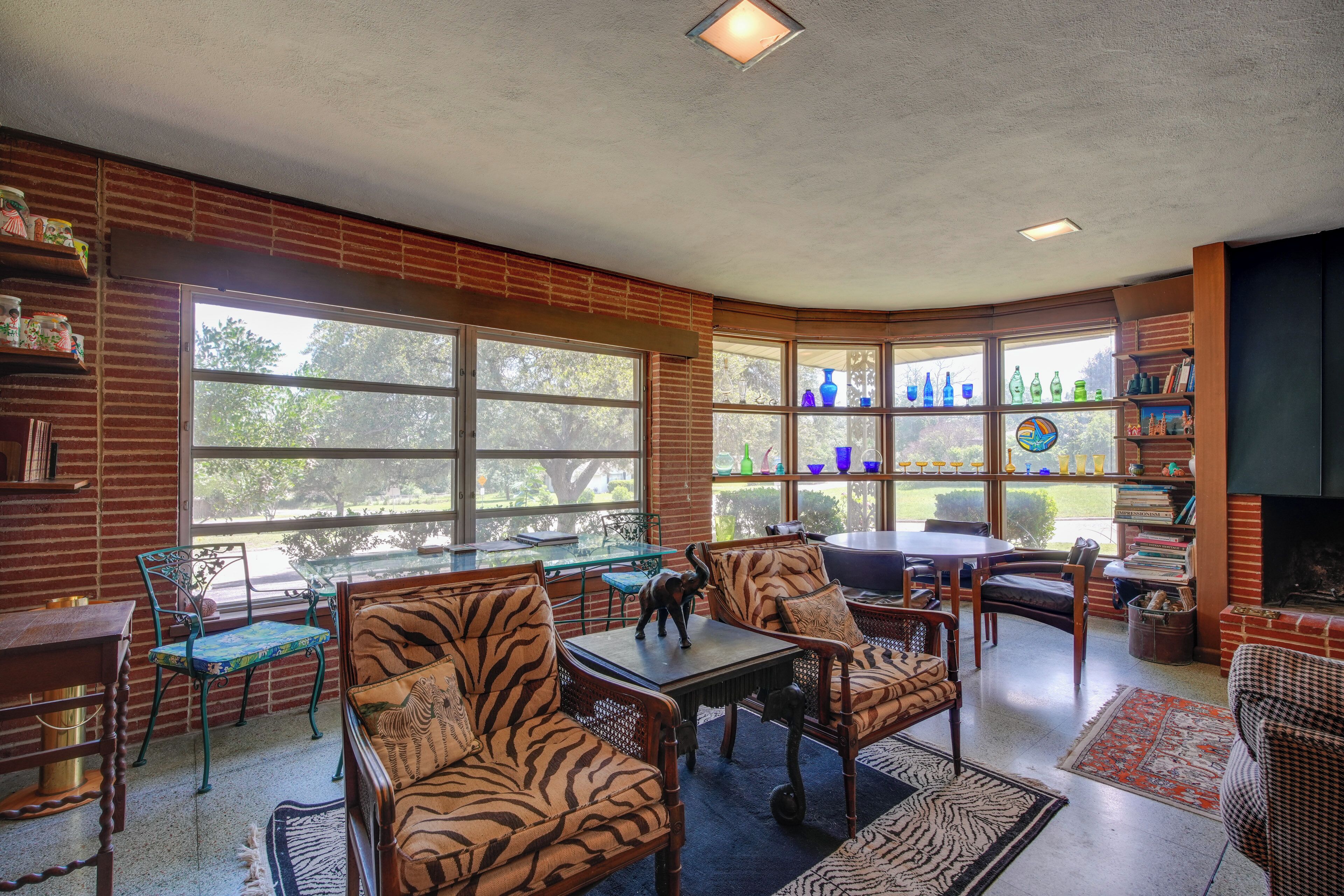 A room with a brick wall, large windows, a fireplace, and zebra-patterned furniture.
