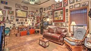 A cozy living room with a leather sofa, a wooden armchair, and a coffee table. The room is decorated with various framed pictures and memorabilia. - San Antonio Rental w/ Courtyard: Walk to Riverwalk (San Antonio)
