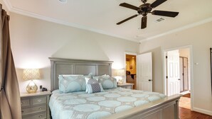 Une chambre à coucher avec un grand lit, deux tables de chevet, un ventilateur de plafond et une porte donnant sur une autre pièce.