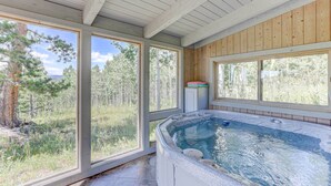 Un jacuzzi en una habitación con ventanas amplias que dan a un bosque.