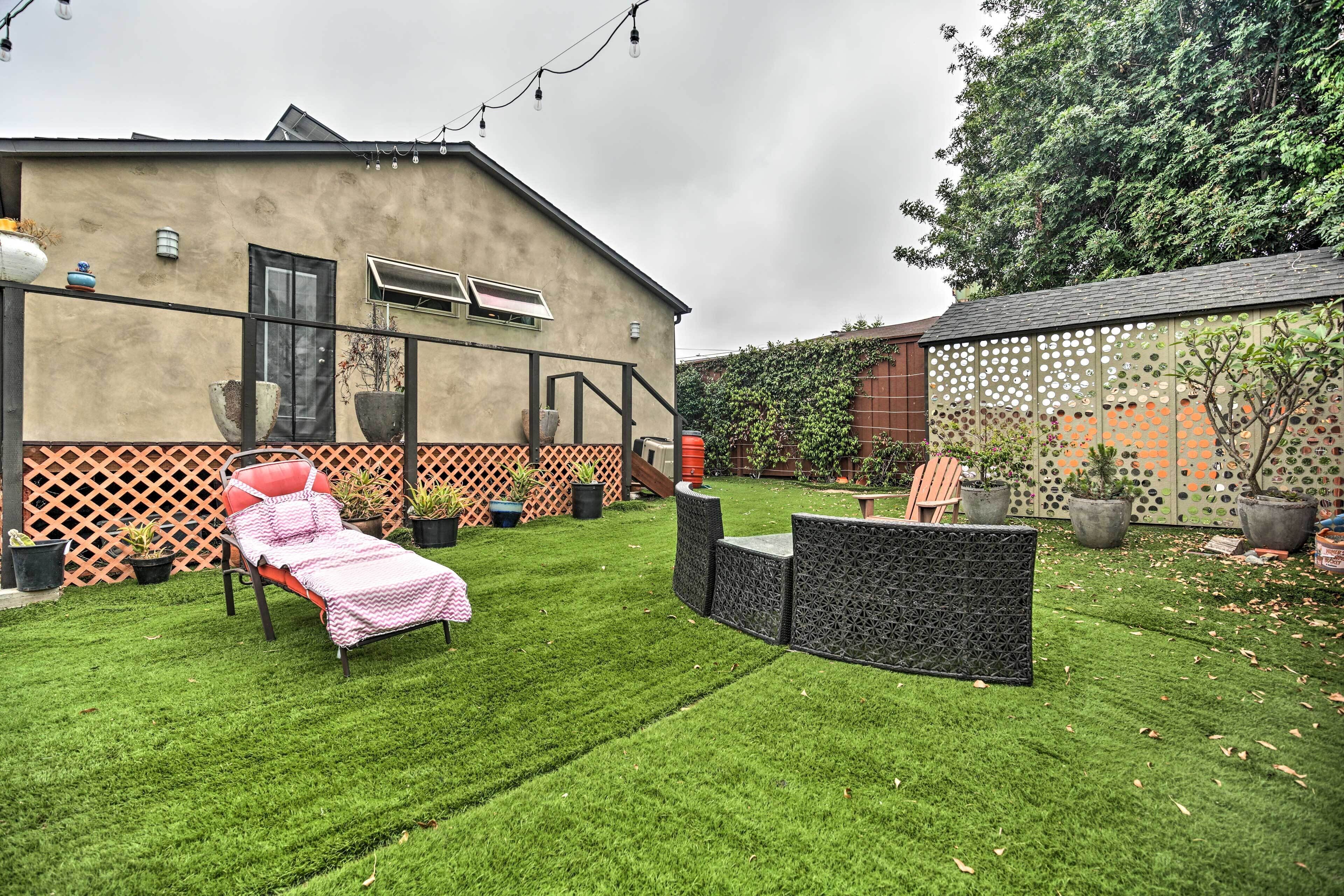 Un jardin avec un parterre de fleurs, des meubles d’extérieur, des plantes en pot et une maison entourée d’une clôture à treillis.