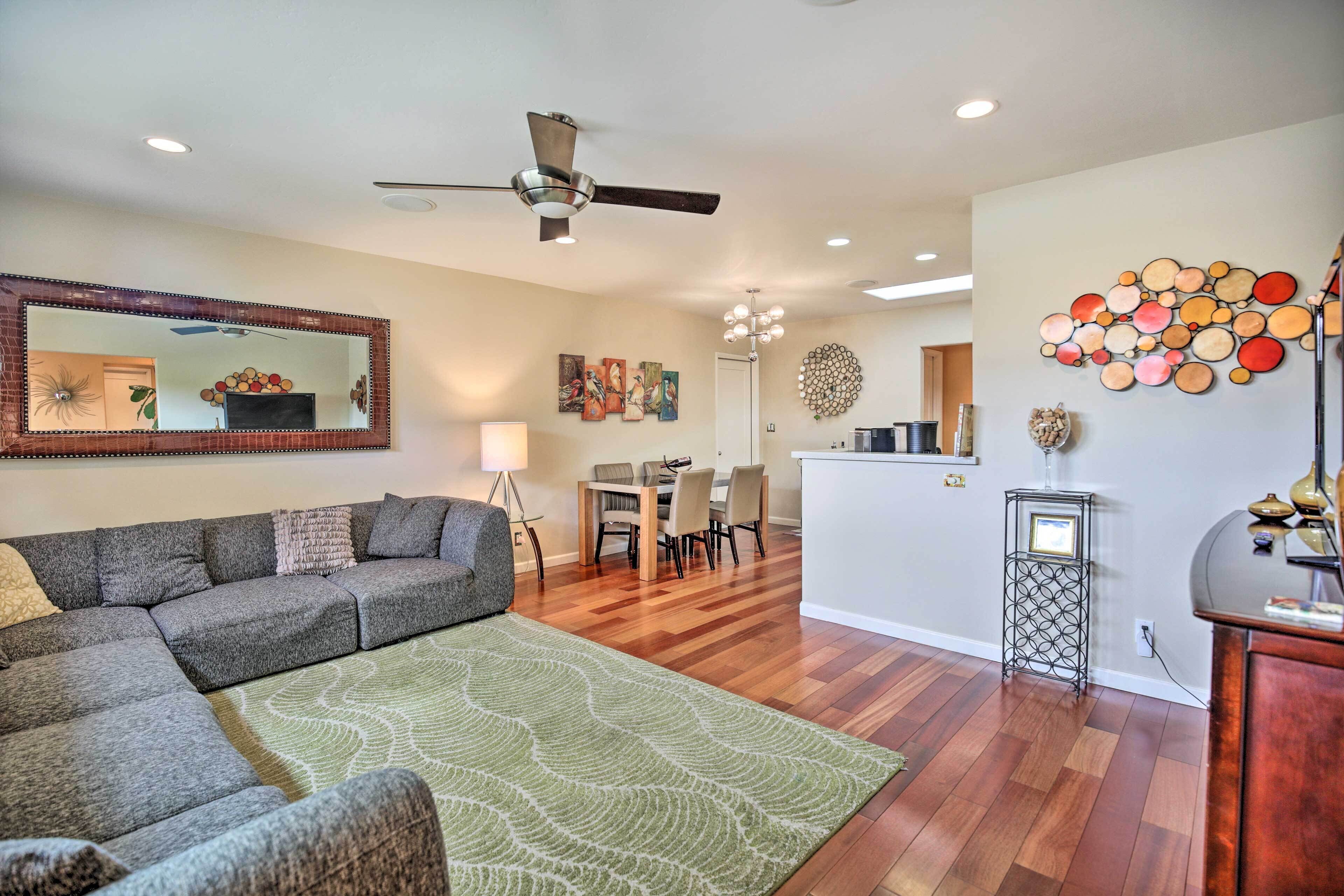 A living room with a sectional sofa, a dining area, a kitchen, and a ceiling fan.