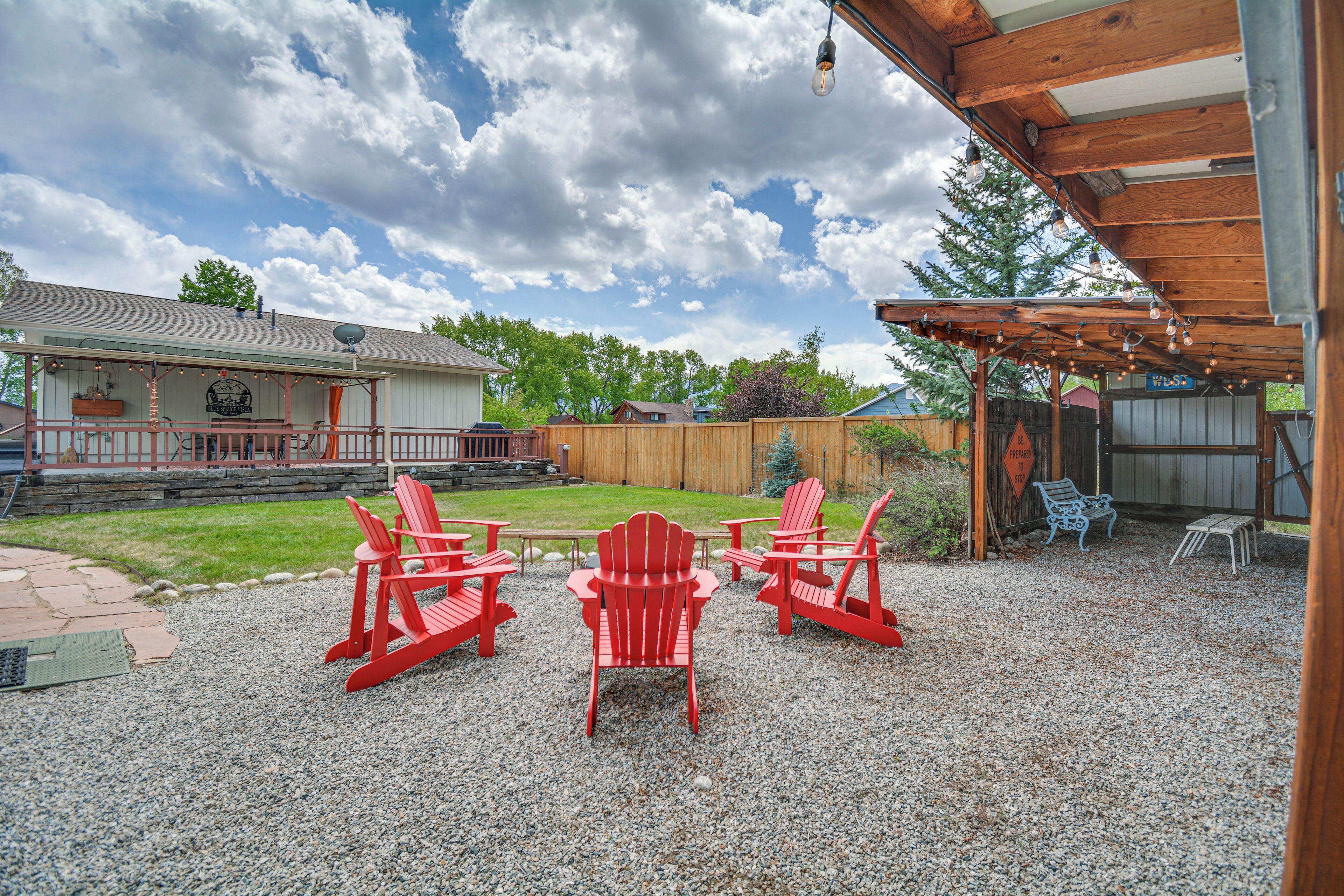Ein Garten mit roten Adirondack-Stühlen, einer Holz-Pergola und einer Kiesterrasse.