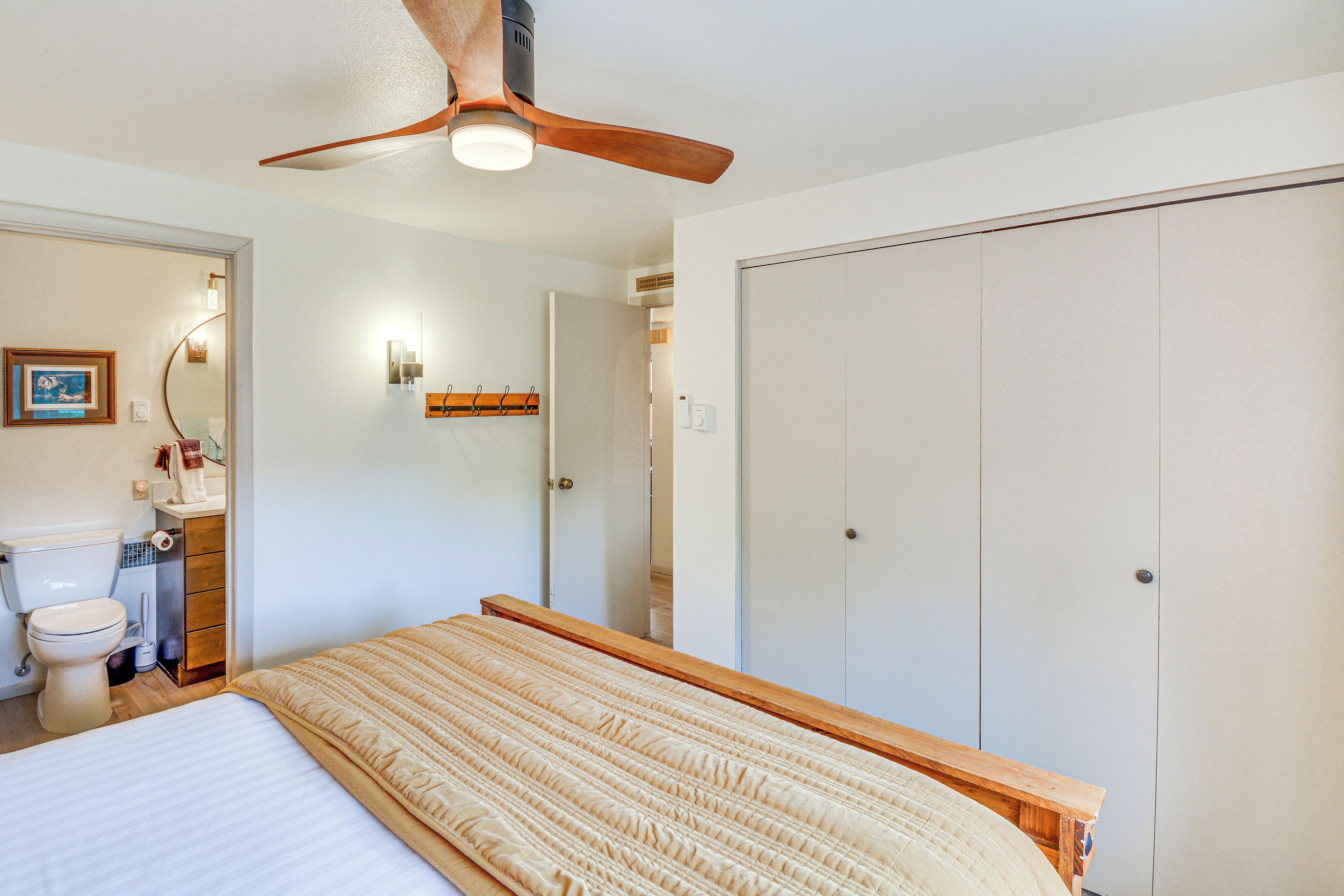 A bedroom with a bed, a ceiling fan, a wardrobe, and a bathroom visible through an open door.