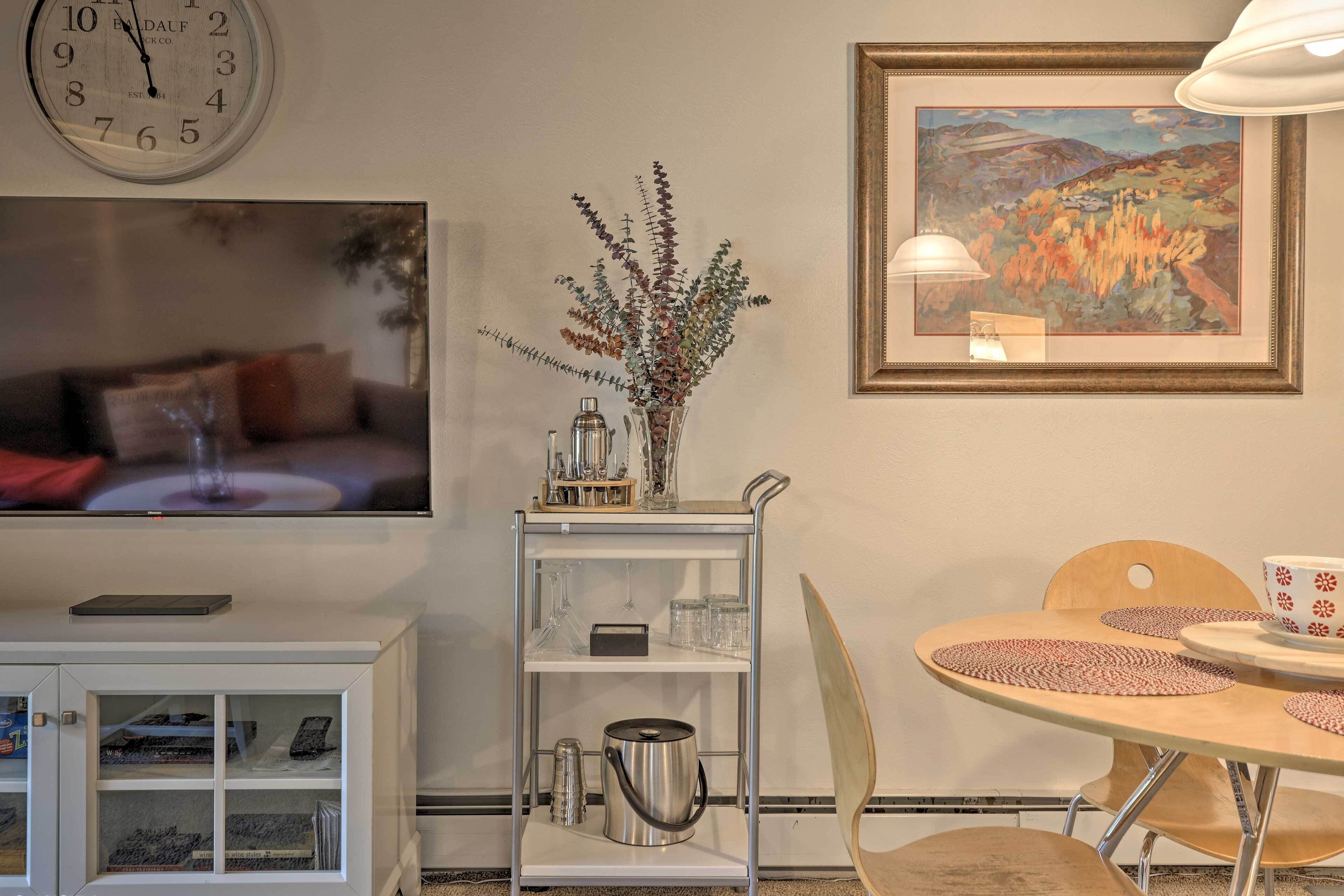 A living room with a white sofa, a coffee table, a bookshelf, a clock, a framed painting, and a vase with dried plants.