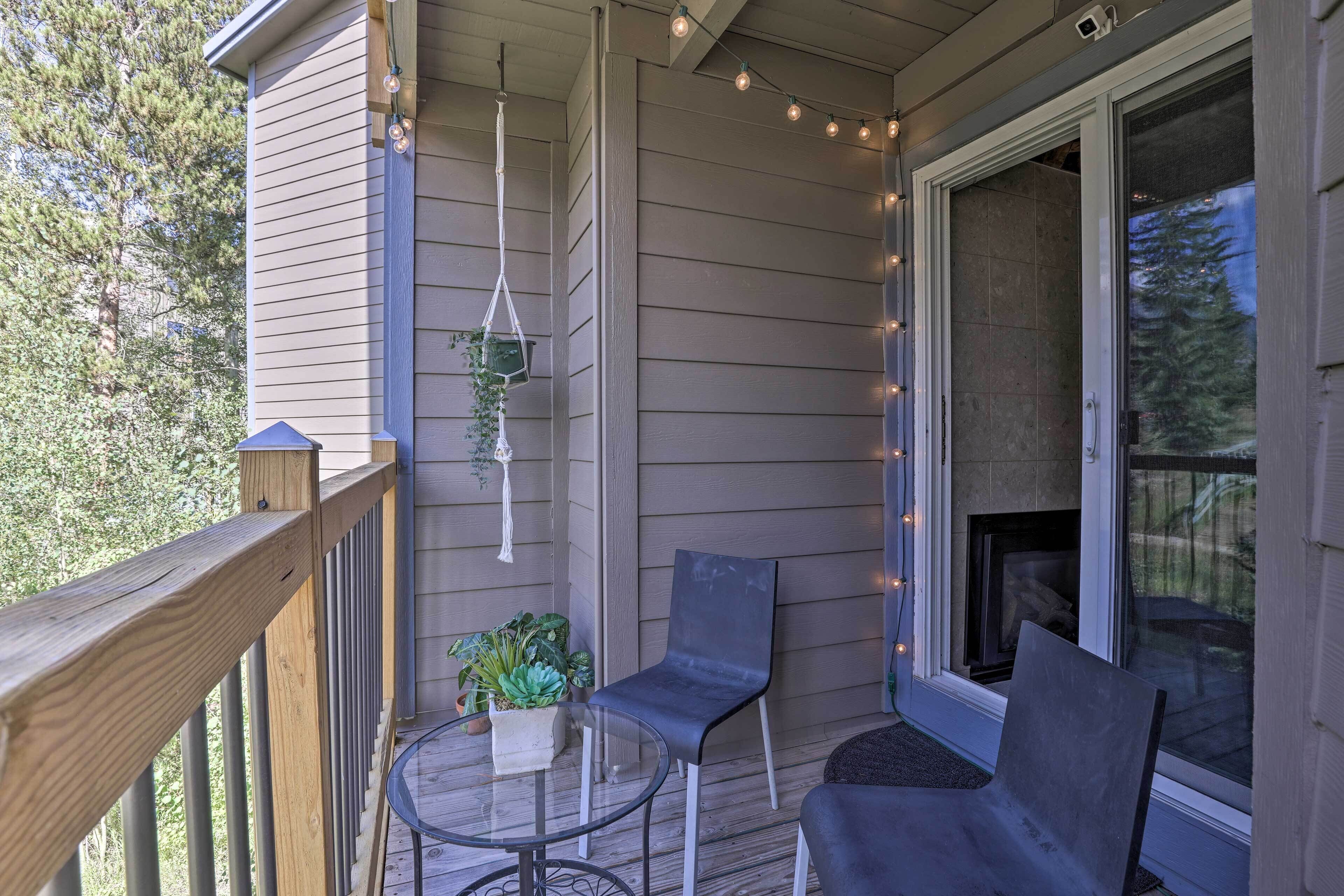 A covered porch with two chairs, a small table, and string lights.