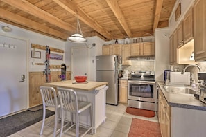 A modern kitchen with wooden beams, stainless steel appliances, and a small dining area with white chairs. - Ski Shuttle & Pool: Modern Silverthorne Condo! (Silverthorne)