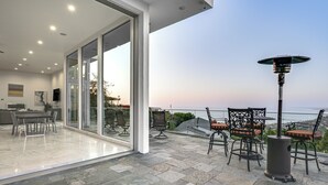 Une terrasse moderne dotée d’un espace repas, d’une grande porte vitrée donnant sur un balcon et offrant une vue sur l’océan.