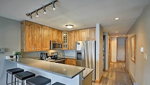 A modern kitchen with wooden cabinets, stainless steel appliances, and a bar area with stools. - Mtn-view Condo w/ Hot Tub Access in Dillon! (Dillon)