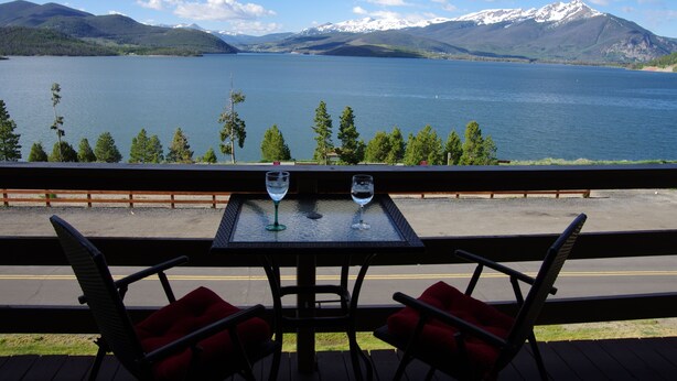 A table with two chairs and two wine glasses on a balcony overlooking a lake with mountains in the background. - Mtn-view Condo w/ Hot Tub Access in Dillon! (Dillon)
