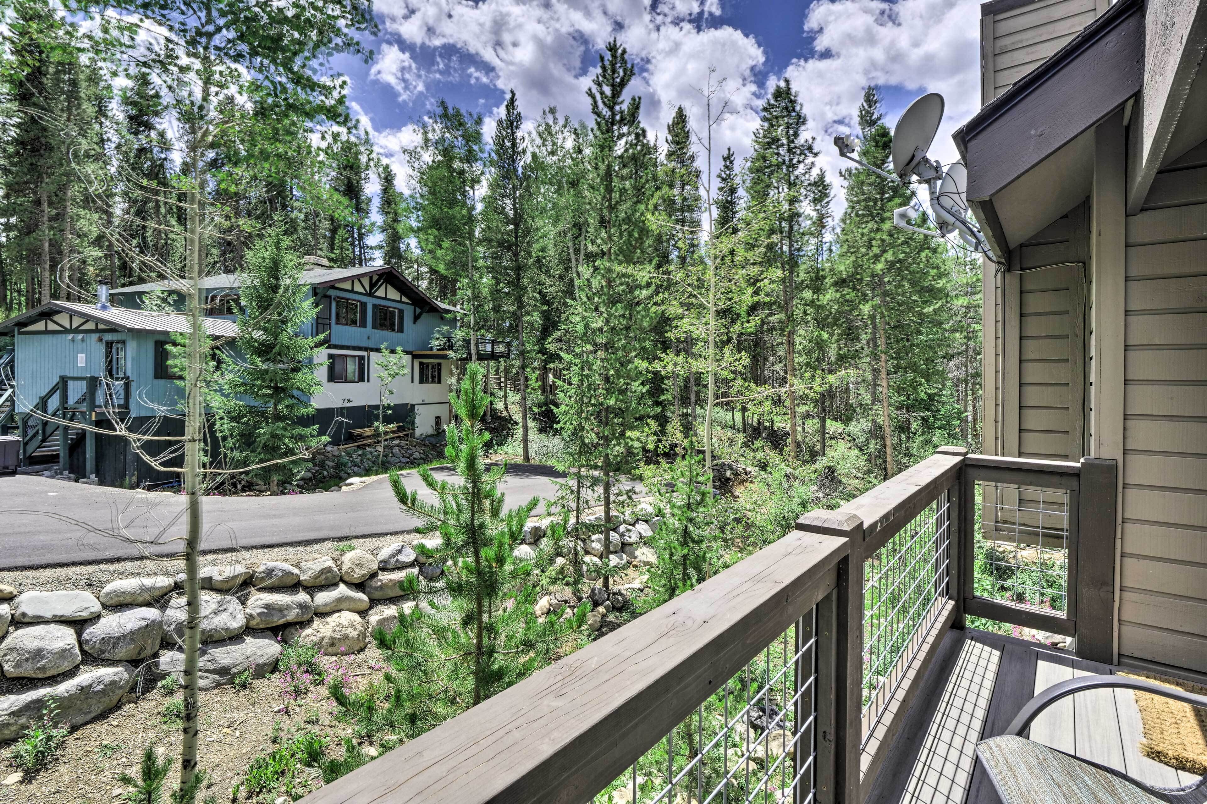 Une terrasse en bois avec une rambarde en métal, donnant sur une zone boisée sous un ciel dégagé.