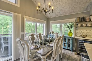 A dining area with a wooden table set for six, surrounded by chairs, with a chandelier overhead and a view of greenery outside. - Upscale Home w/ Hot Tub: 3 Mi to Breck Ski Resort! (Breckenridge)