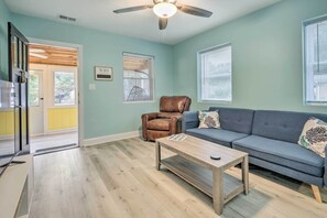 A living room with a sofa, a coffee table, a leather chair, and a ceiling fan. - Updated North Beach Cottage: Pet Friendly! (North Beach)