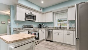 A modern kitchen with white cabinets, stainless steel appliances, and a granite countertop. - Updated North Beach Cottage: Pet Friendly! (North Beach)