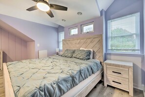 A bedroom with a bed, a nightstand, a ceiling fan, and a window with blinds. - Updated North Beach Cottage: Pet Friendly! (North Beach)