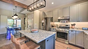 A modern kitchen with granite countertops, stainless steel appliances, and a central island with bar stools. - Modern Home w/ Patio Near Garden of the Gods! (Colorado Springs)