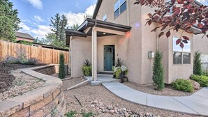 A modern house with a covered porch, a stone retaining wall, and a landscaped garden with various plants. - Modern Home w/ Patio Near Garden of the Gods! (Colorado Springs)