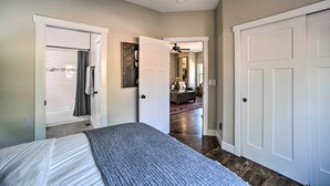 A bedroom with a bed, a door leading to a bathroom, and a hallway with a ceiling fan. - Modern Home w/ Patio Near Garden of the Gods! (Colorado Springs)