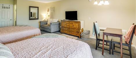 A bedroom with two beds, a dresser, a TV, a chair, and a table.