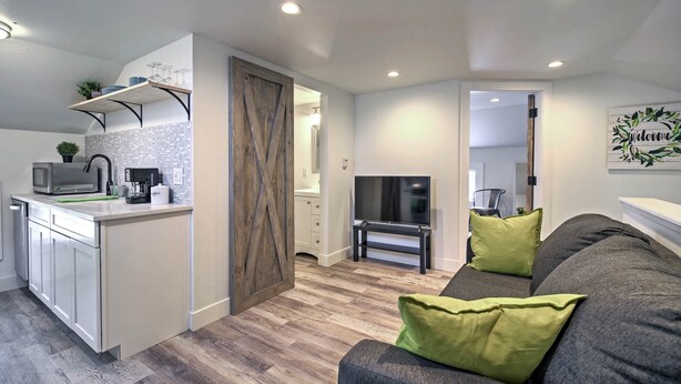 A modern kitchen with white cabinets, a built-in microwave, and a coffee machine. There is a TV on a stand and a sofa with green cushions in the living area. - Dtwn Golden Apt < 9 Mi to Red Rocks Amphitheater! (Golden)