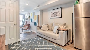 A modern living room with a beige sofa, a grey rug, and a stainless steel refrigerator.