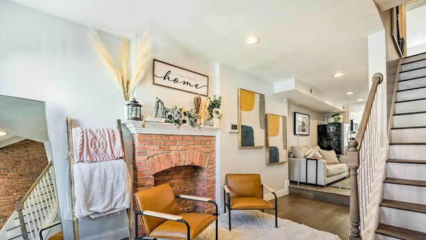 A modern living room with a brick fireplace, leather chairs, a white fluffy rug, and a staircase.