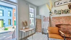 A modern living room with a brick fireplace, large windows, and a view of the street.