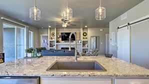 A modern kitchen with a granite countertop, stainless steel sink, and pendant lights.