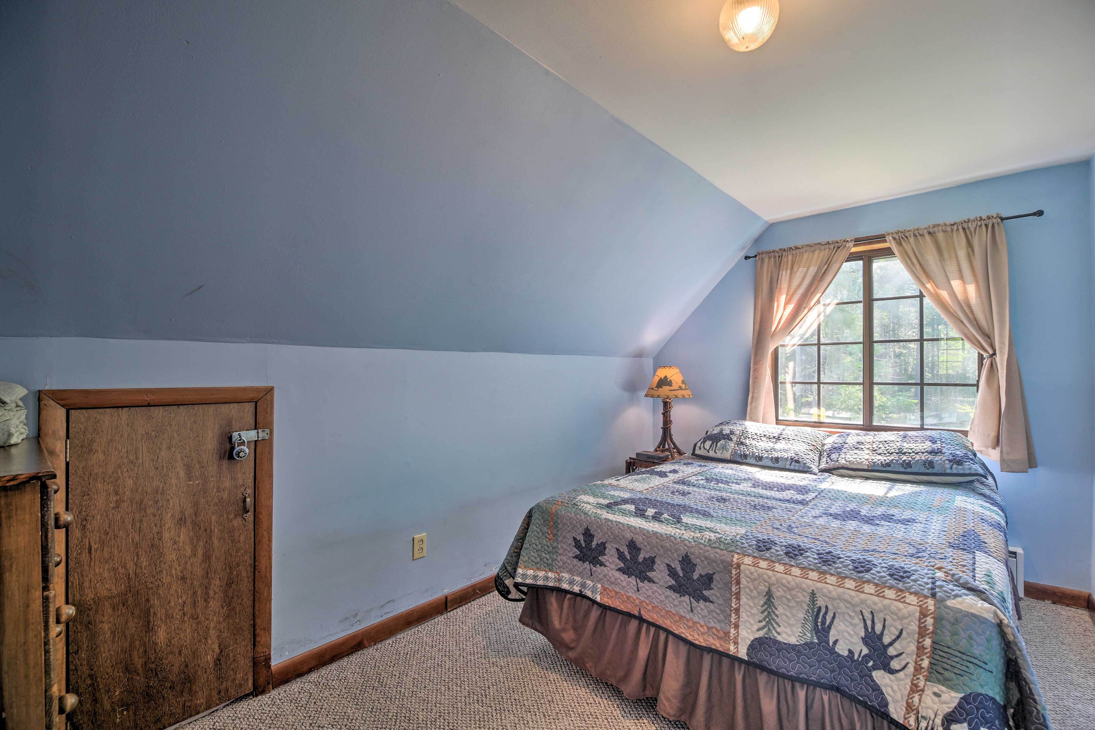 A bedroom with a bed, a window with curtains, a lamp, and a door.