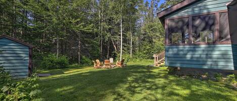 Una cabaña con terraza y zona de estar al aire libre, rodeada de un bosque denso.
