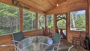 Una baita di legno con un tavolo e sedie in vetro, ampie finestre e vista sulla foresta.