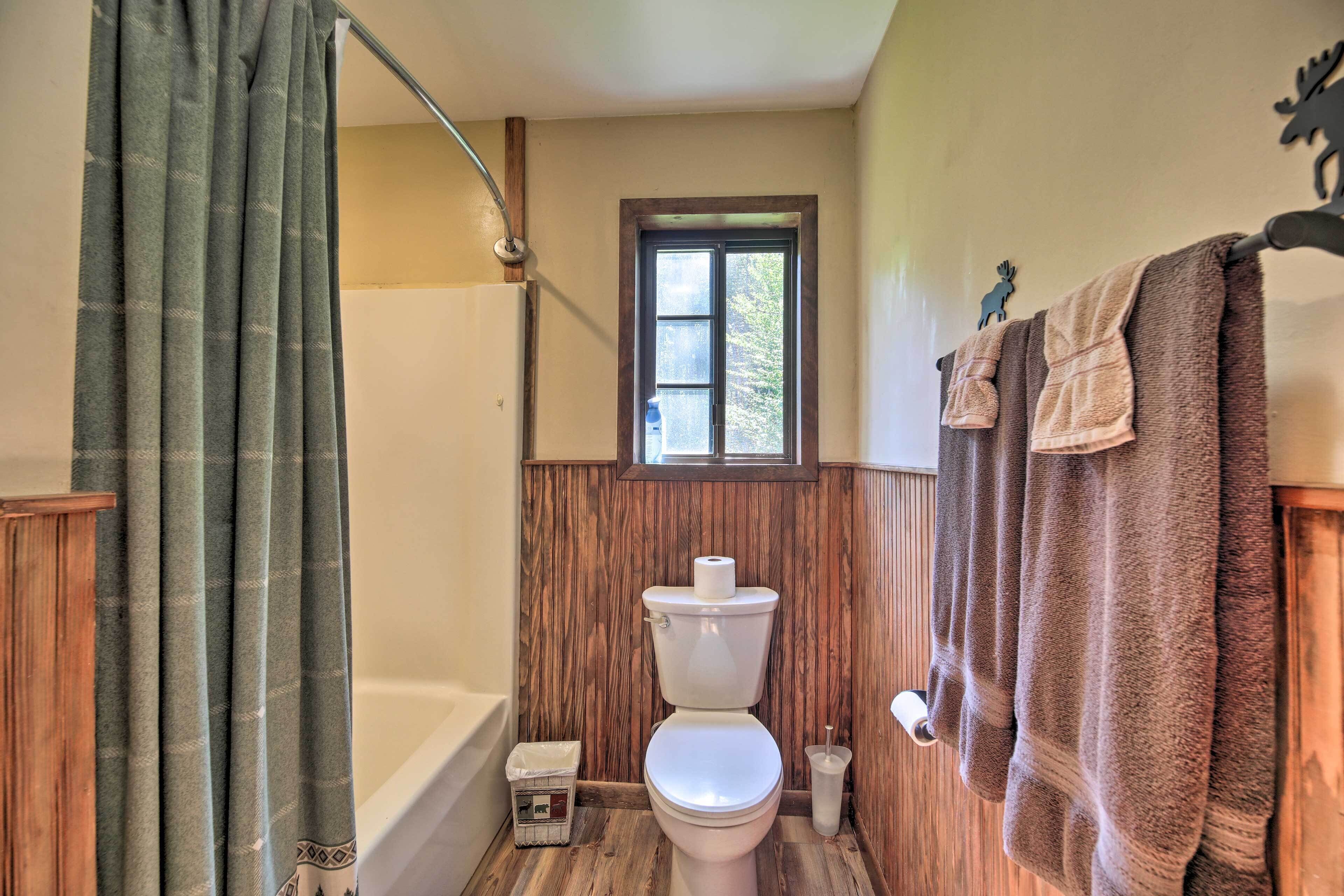 A bathroom with a wooden floor, a white toilet, a bathtub, and a shower curtain.