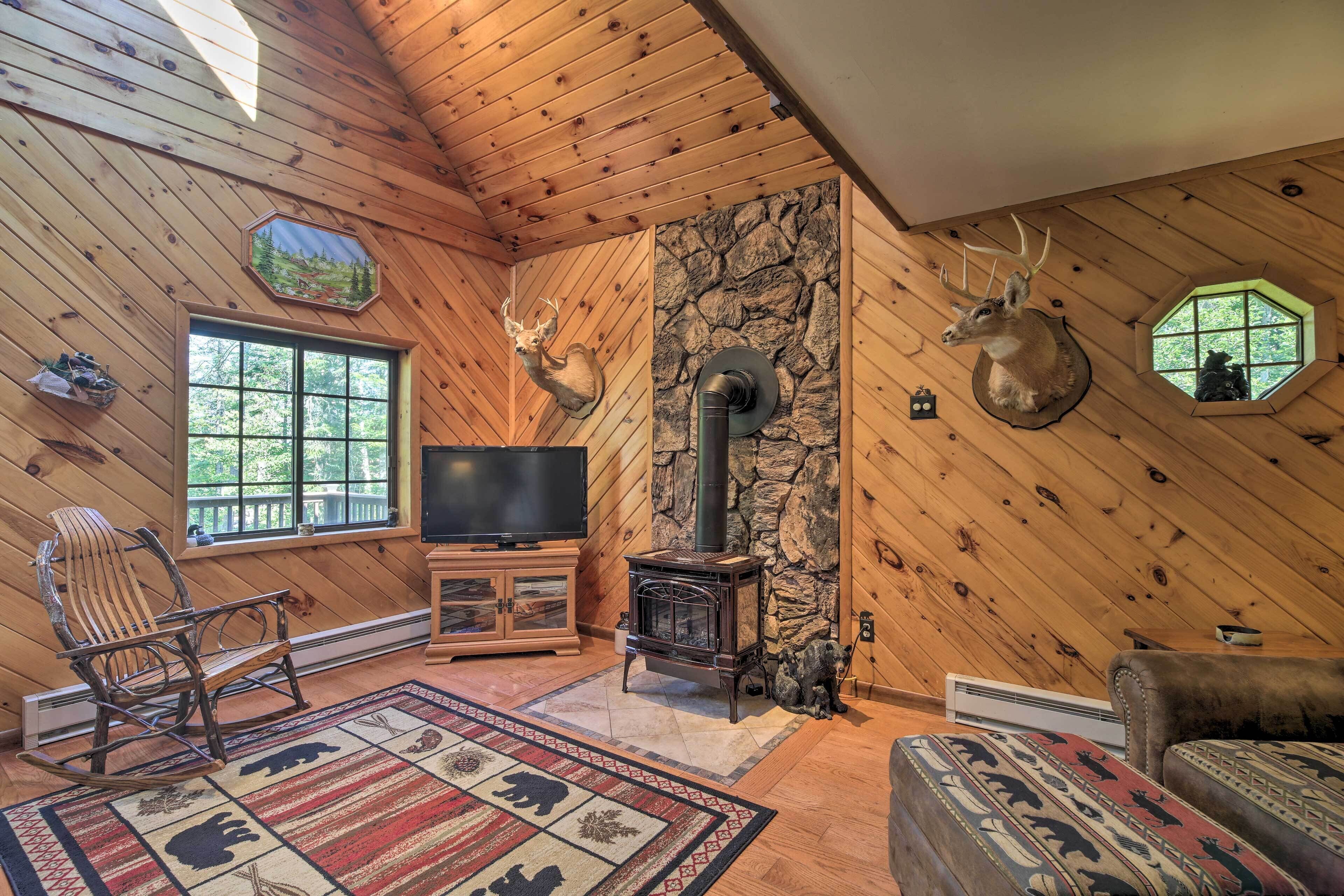A cozy cabin interior with wooden walls, a stone fireplace, a television, and deer head decorations.