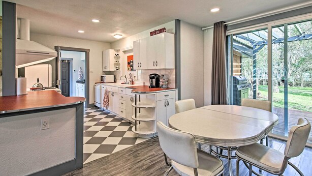 Una cocina moderna con armarios blancos, una isla central y una zona de comedor con una mesa redonda y sillas.